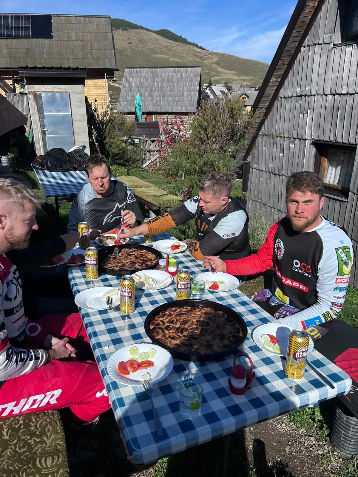 Enduro-Fahrer beim gemeinsamen Mittagessen an einem Holztisch bei einer Berghütte