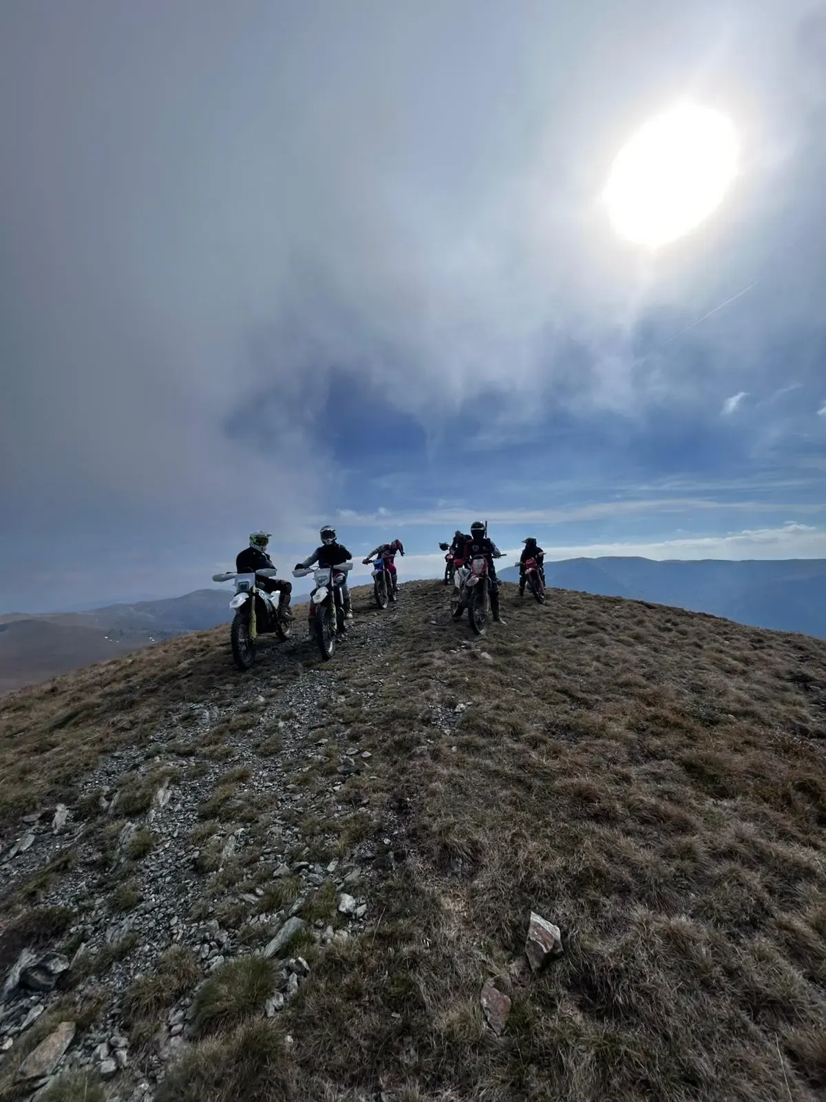Enduro-Gruppe mit Motorrädern auf einem Berggipfel unter dunklen Wolken