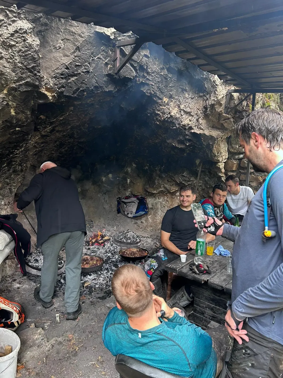 Enduro-Gruppe beim Essen an einer Feuerstelle unter einem Felsüberhang