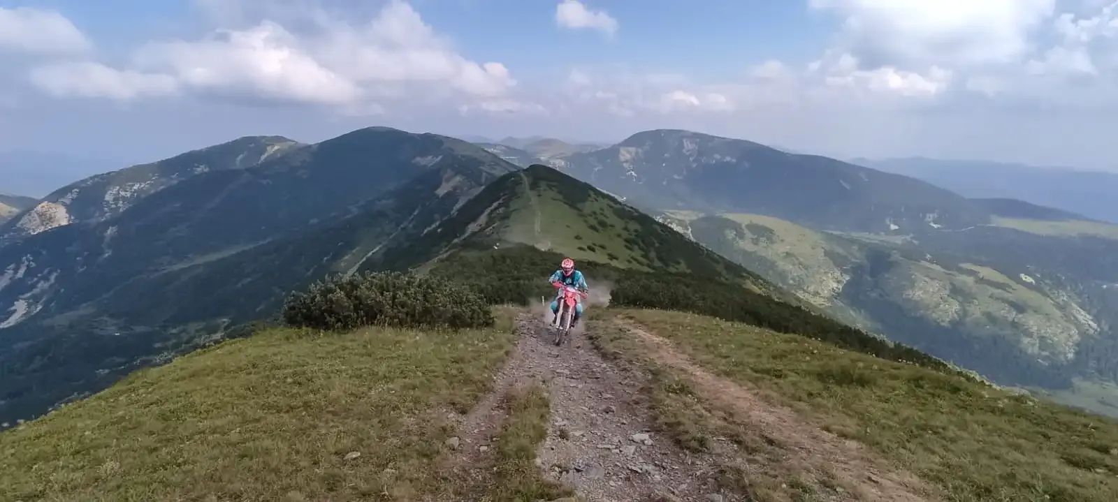 Enduro-Fahrer auf einem Bergpfad entlang eines grünen Höhenrückens